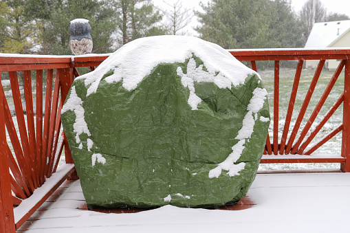 A gas grill protective cover in the winter covered with snow