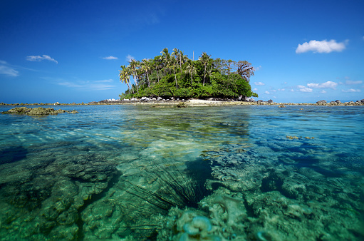 A scenic view of Koh Pling (Pling Island) on clear blue sky and water with sea urchin and coral reefs in rippled water during low tide. A  hidden  small island viewpoint near Nai Yang Beach in Sirinat National Park. A tropical holiday escape, Phuket, Thailand.