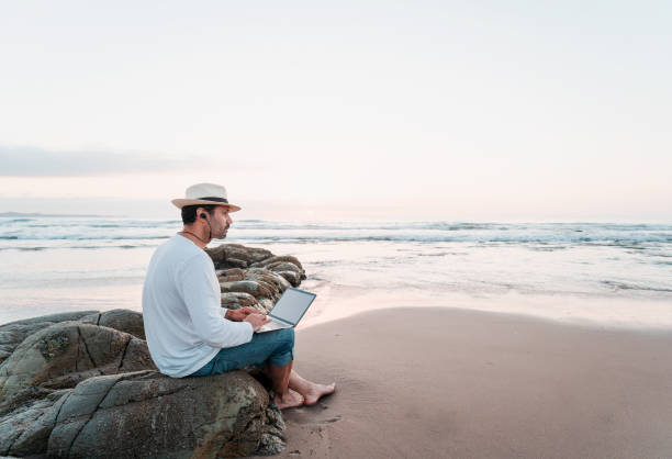 istock latin man sitting on the beach with a laptop alone at sunset 1363707587
