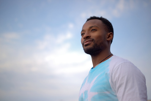 young african man wearing tie and dye t-shirt on blue cloudy sky spiritual portrait