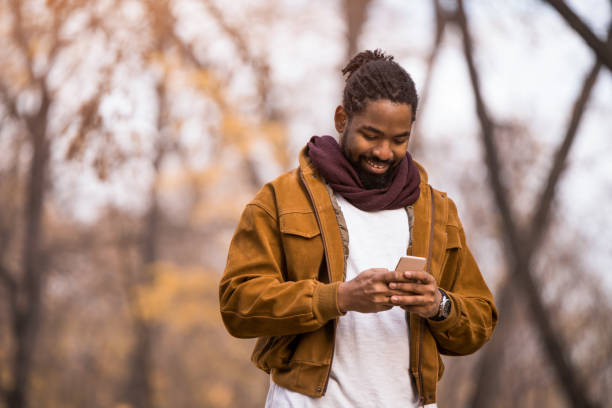 istock Happy African American man using phone while walking in autumn park. 1363710043