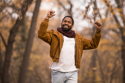 Cheerful African American man celebrating and running in nature on beautiful autumn day.