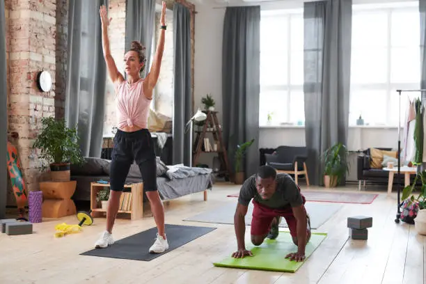 Horizontal wide shot of sporty young man and woman exercising in morning in loft living room at home