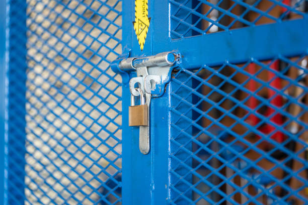 A key padlock is locking on metal fence gate knob of the hand tool storage box (as blurred backgroung). Industrial object photo. Close-up and selective focus.