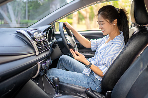 Portrait of a young woman texting on her smartphone while driving a car. Business woman sitting in car and using her smartphone.