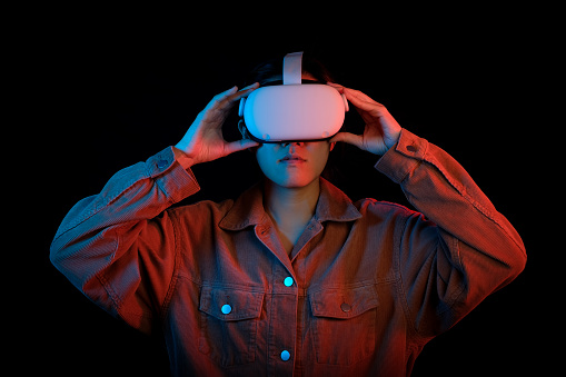 Young women holding VR headset on black background. The neon theme for futuristic education and gaming via meta verse.