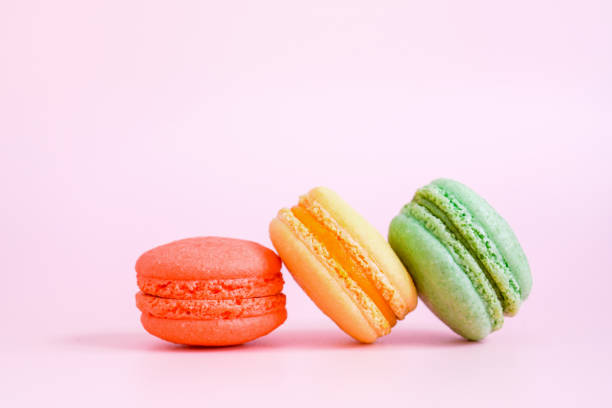three colored sweet homemade macarons on sweet pink background, close up stock photo