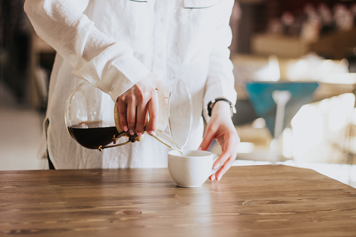 Una chica con una camisa blanca vierte café en la papilla. Chemex. Formas alternativas de preparar café. Concepto de cafetería photo