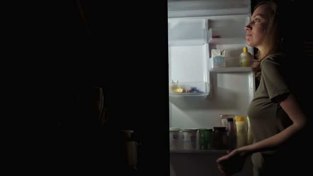 Woman take apple from refrigerator at night