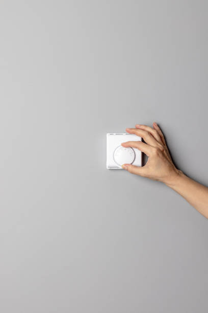 Botón del controlador del regulador de temperatura de la pared que ajusta o apaga la mano de la mujer - foto de stock
