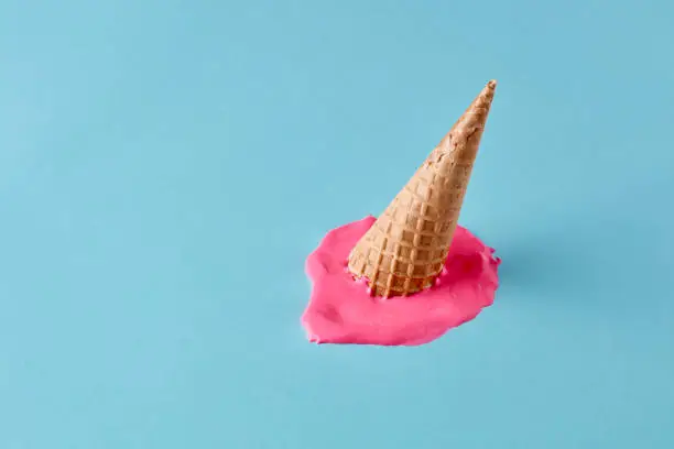 Photo of Dropped upside down ice cream cone with melting scoop on pastel blue floor. Minimalistic summer food