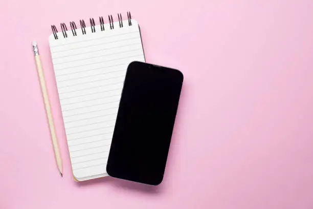 Smartphone and spiralnotebook isolated on pink background