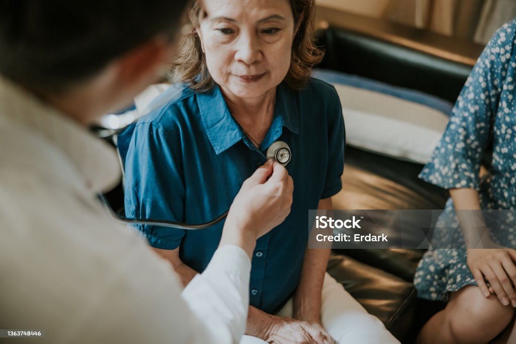 Close-up, Asian Doctor concentrate on listening heartbeat of senior woman. Asian Male doctor using a stethoscope to examining senior woman's lung and heartbeat during a healthcare home visit. Lung Cancer Stock Photo