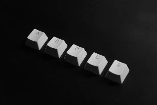 Photo of A,b,c,d,e alphabets letters on white keyboard keycaps on dark wood background, illustration.