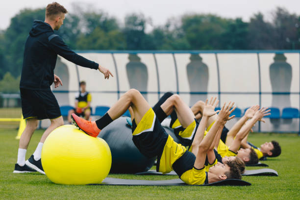 fußballspieler: stretching-session mit physiotherapeut. jugendsportmannschaft in der erholungssitzung nach dem ligaspiel. fußballspieler wärmen sich auf dem rasenstadion auf - warming up fotos stock-fotos und bilder