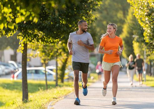 Smiling man and woman talking with each other while running in a public park.