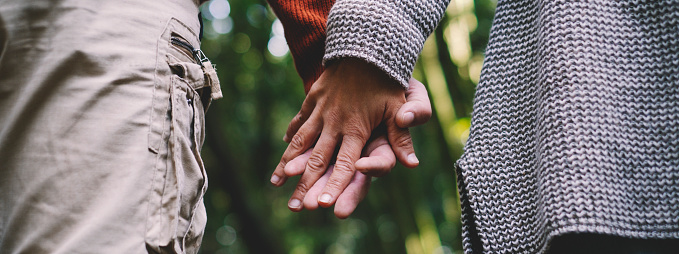 Banner header Close up of man and woman couple hands holding each other together with love and relationship and green woods nature forest in background - concept of friendship and healthy lifestyle