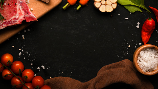 Copy space on a black background surrounded with raw steak and steak's seasoning and fresh vegetable. Raw steak background. top view, overhead.