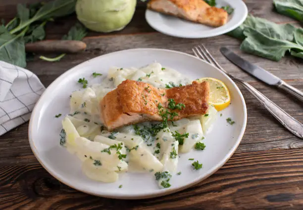 Homemade traditional fish dish with pan fried salmon fillet served with kohlrabi in a delicious bechamel sauce on a plate on rustic and wooden table