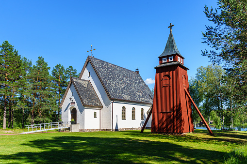 Beautiful white countryside church in Sweden with a separate red clocktower, in summer sunlight and a clear blue sky