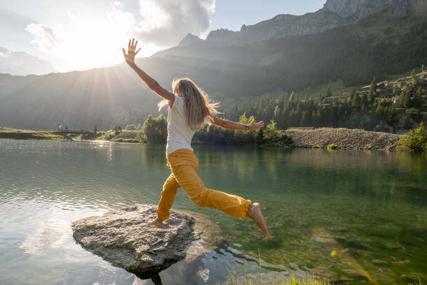 l'escursionista femmina salta da una roccia all'altra sopra il lago alpino - european alps women summer outdoor pursuit foto e immagini stock
