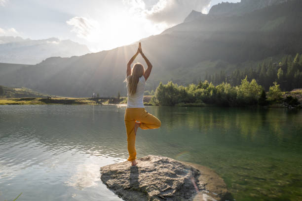 une jeune femme fait du yoga sur un rocher au-dessus du lac au lever du soleil - mountain rock sun european alps photos et images de collection