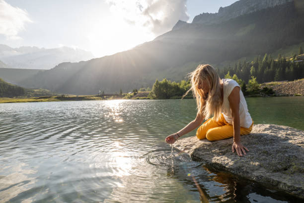 istock Young woman scooping water from alpine lake 1363758489