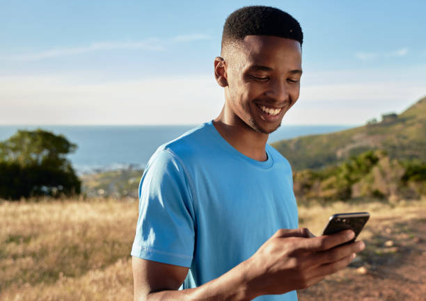 istock Black young Adult male smiling while using his cellphone, about to start mountain walk. Beautiful outdoors activity 1363758550