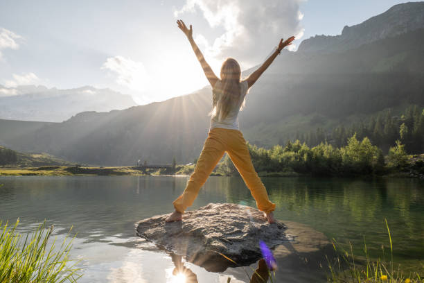 une jeune femme s’arrose sur un rocher au-dessus du lac alpin au lever du soleil, concept de bonne matinée - mountain rock sun european alps photos et images de collection