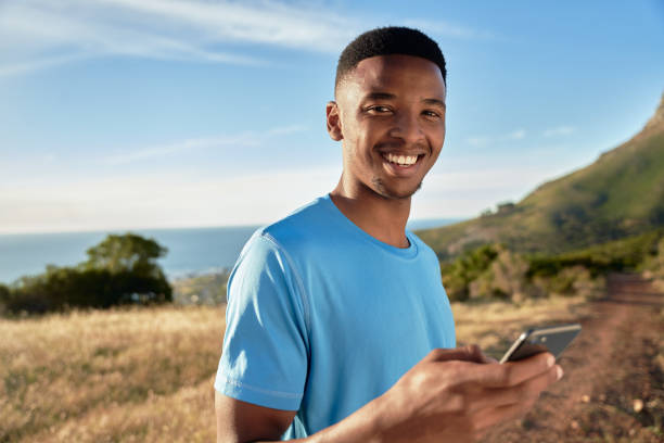 retrato de un hombre adulto joven negro sonriendo a la cámara mientras usa su aire libre en la montaña a punto de comenzar a correr - ewan fotografías e imágenes de stock