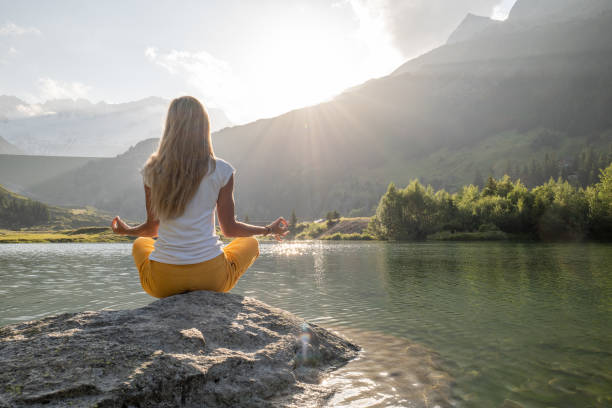 istock Young woman meditating on rock above lake 1363758730