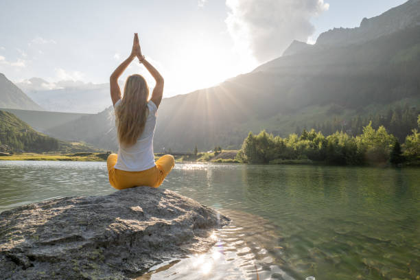 jeune femme méditant sur un rocher au-dessus du lac - mountain rock sun european alps photos et images de collection