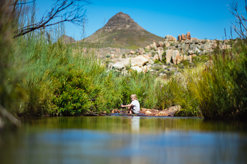 A young 8-9 year old beautiful Caucasian cute Girl playing in fresh mountain stream in the wilderness on a hot summers day.  There is a mountain peak called Sugarloaf in the Cederberg Mountains behind her.  She has blond hair and is enjoying herself.