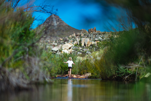 Rear view of a A young 8-9 year old beautiful Caucasian cute Girl playing in fresh mountain stream in the wilderness on a hot summers day.  There is a mountain peak called Sugarloaf in the Cederberg Mountains behind her.  She has blond hair and is enjoying herself.