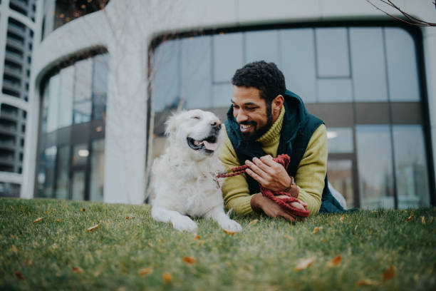 Happy young man lying on grass with his dog outdoors in town.