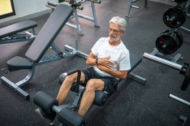 Senior man in late 60s doing crunches while having a workout in the gym Senior Caucasian man in late 60s doing bench crunches for strong abs and lower body while having a workout in the gym to stay fit and healthy during his retirement senior bodybuilders stock pictures, royalty-free photos & images