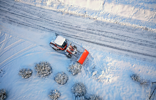 Snow removing with red tractor on the road. Suny winter day, Drone top view. Aerial. View from above.