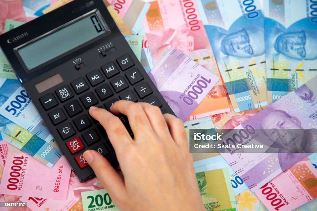hand typing on calculator in paper currencies background Indonesian Currency Stock Photo