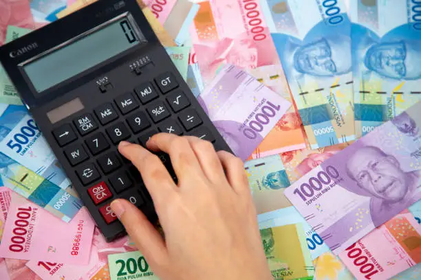 Photo of hand typing on calculator in paper currencies background