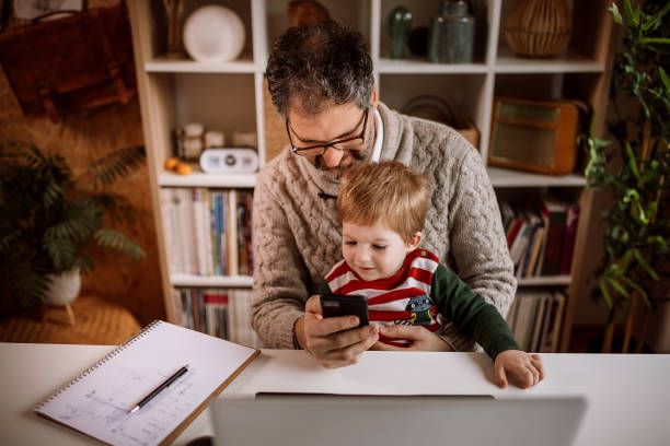 istock Working father watching cartoon with his son on mobile phone while working 1363764798