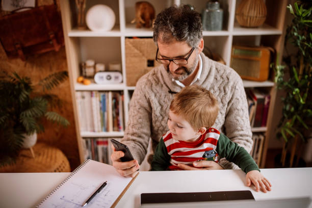 istock Working father watching cartoon with his son on mobile phone while working 1363764887