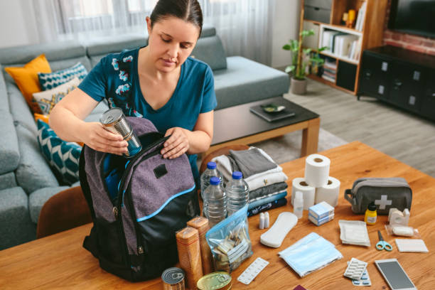 woman putting cans of food to prepare emergency backpack - deprem stok fotoğraflar ve resimler