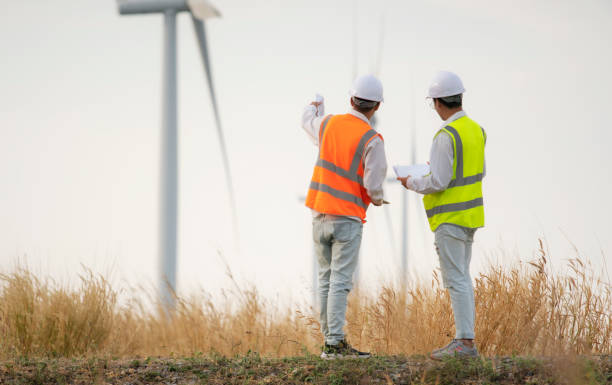 dwóch azjatyckich inżynierów lub techników w mundurach dyskutuje i sprawdza. turbiny wiatrowe ekologiczna energetyka przemysł energetyki wiatraków pracownik terenowy odnawialne tło. - alternative energy electricity wind turbine team zdjęcia i obrazy z banku zdjęć