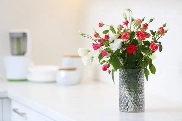 Vase with beautiful flowers on white countertop in kitchen, space for text