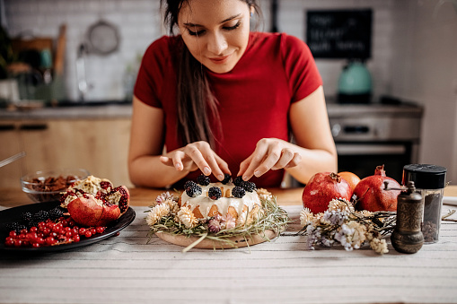 Young beautiful woman decorating her cake with berry fruits