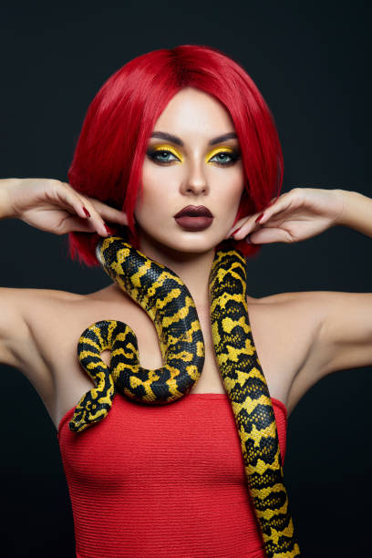 istock Beautiful woman with red hair and a yellow python snake around her neck. Professional Bright Beauty Eye Makeup Yellow, Red Burgundy Lipstick 1363769587