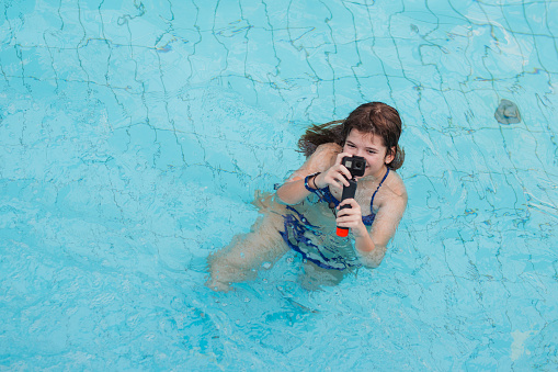 Cheerful young girl having fun with waterproof wearable camera in her hands when swimming in a swimming pool