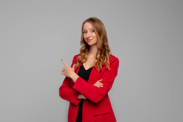 istock confident young woman points finger at upper left corner, showing to the advertisement, looking determined at camera, standing in red blazer against gray background 1363774347