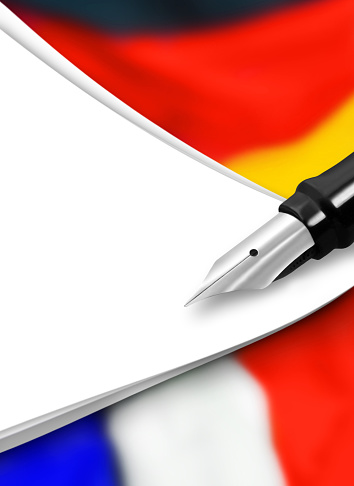 White paper background with German and French national flags and fountain pen closeup
