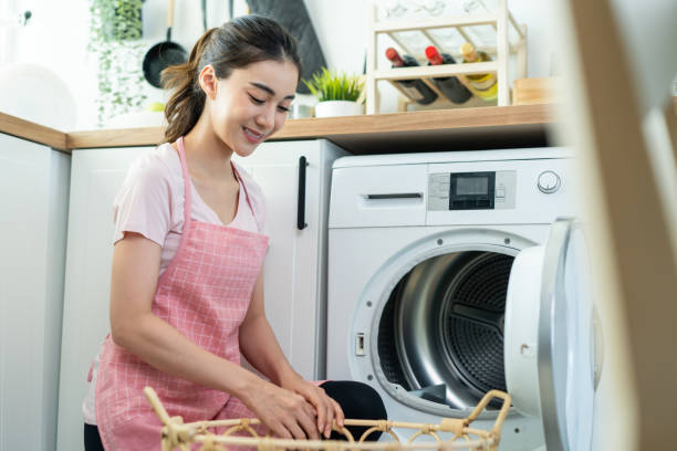 Asian beautiful woman put dirty clothes to washing machine in house. Attractive girl wear apron sit on floor, feel happy to loads laundry in washer appliance at home. Domestic-House keeping concept. la hermosa mujer asiática puso ropa sucia a la lavadora en la casa. chica atractiva usar delantal sentarse en el suelo, sentirse feliz de cargas de lavandería en el electrodoméstico de la lavadora en casa. concepto de mantenimiento de la casa doméstica